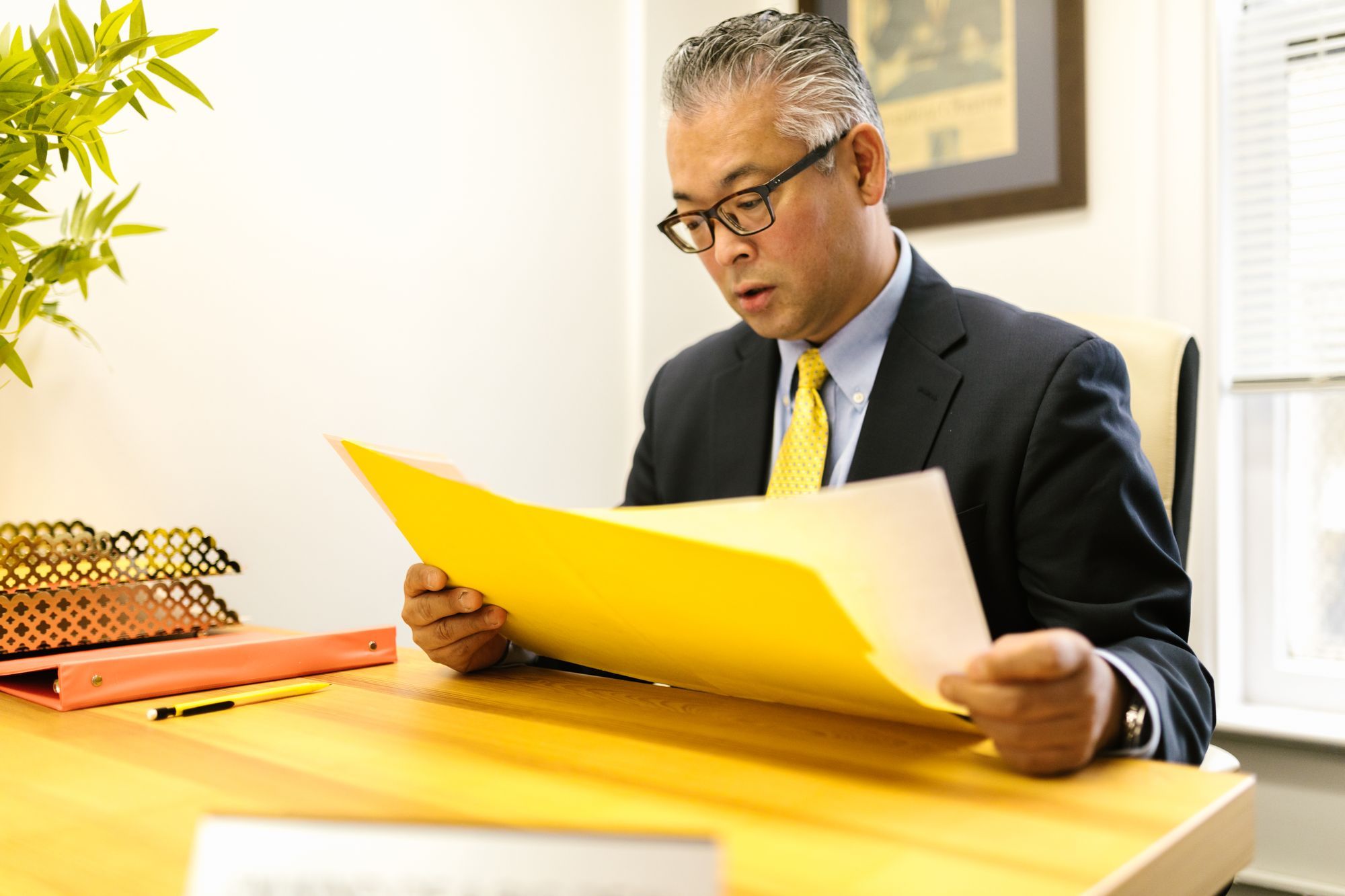 Business owner in a suit reading through a folder of bank loan papers at his office desk