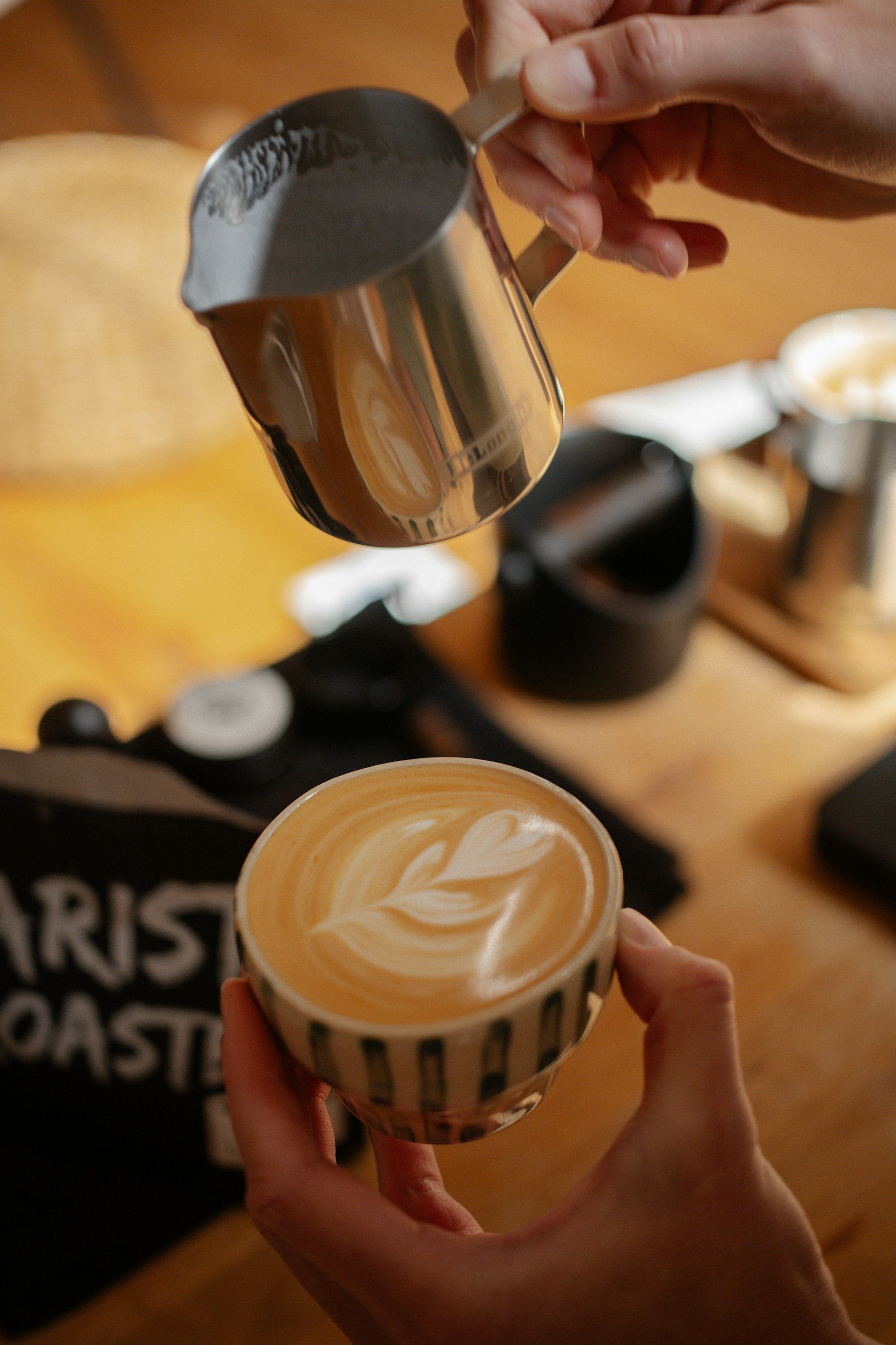 Cafe owner pouring steamed milk to make latte art in a cup of coffee