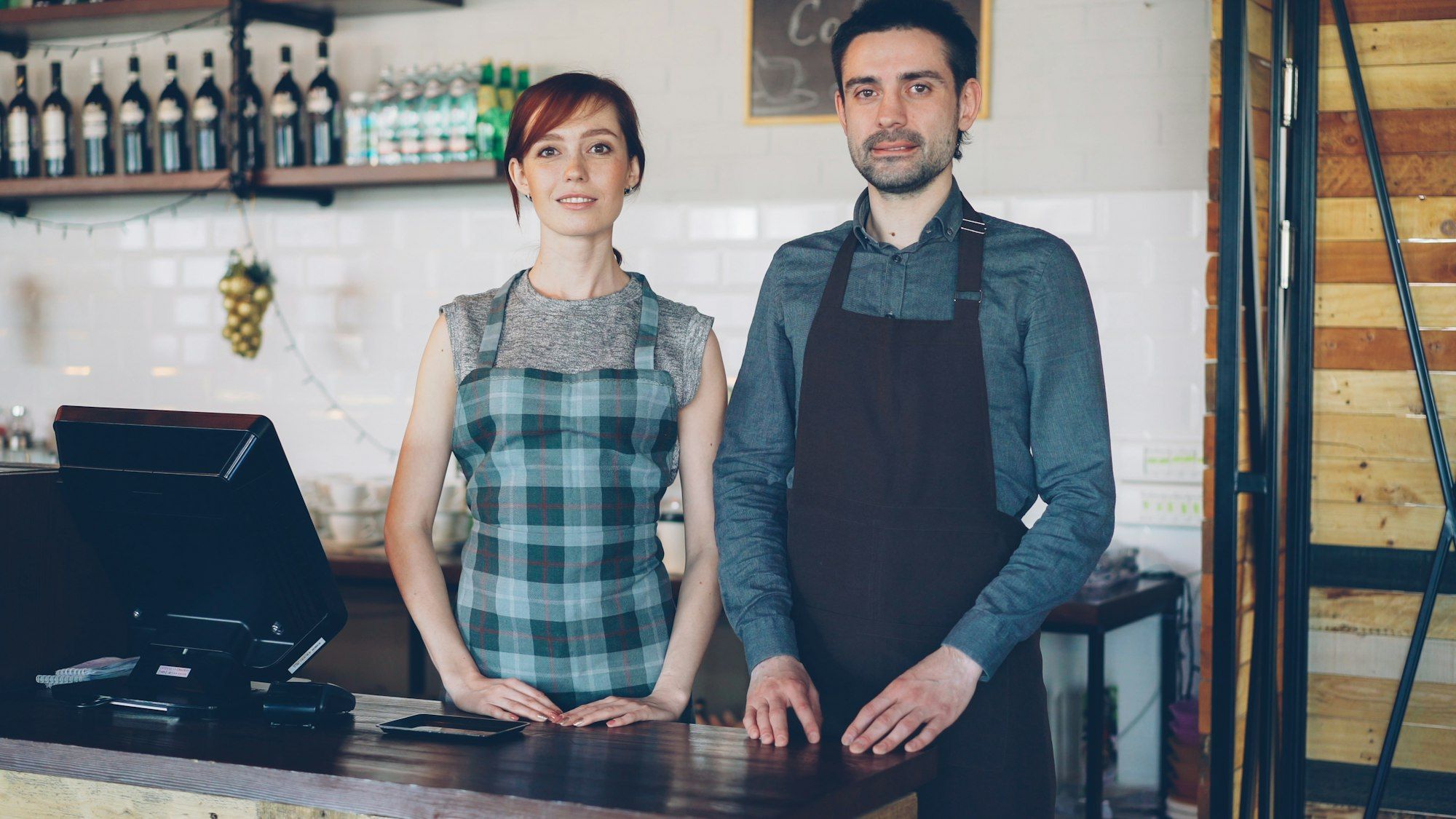 Two cafe staff in aprons standing behind the counter ready for customers